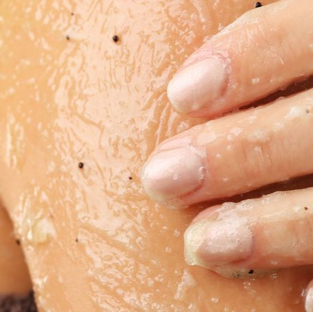 Close-up of a hand touching a shoulder with scrub on skin showing texture.