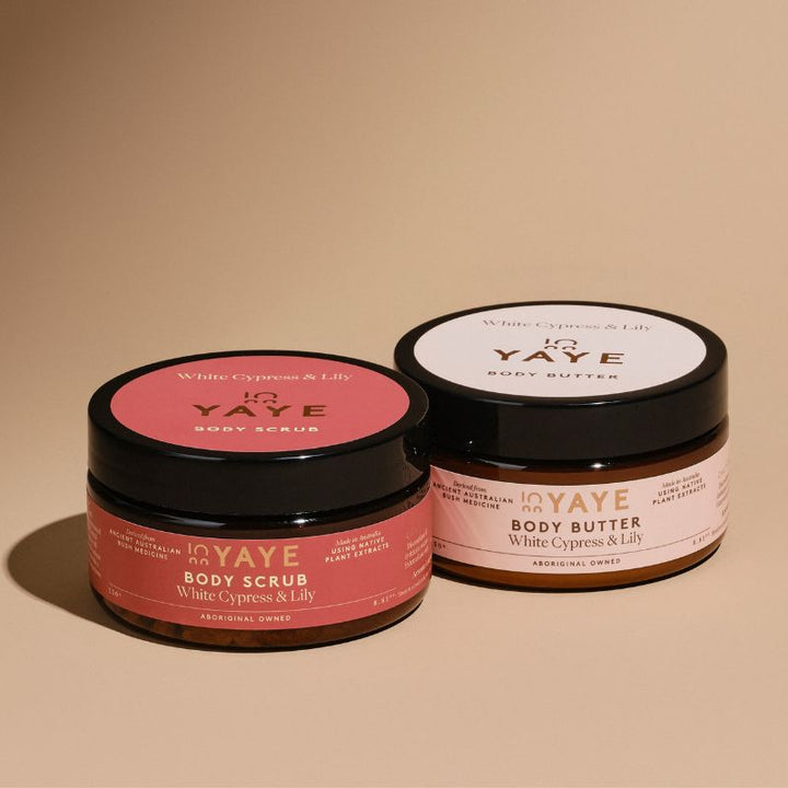 White Cypress & Lily Body Butter and Body Scrub from Yaye’s Glow Bundle displayed side by side, showcasing their clean design and native botanical ingredients in a serene, natural setting.