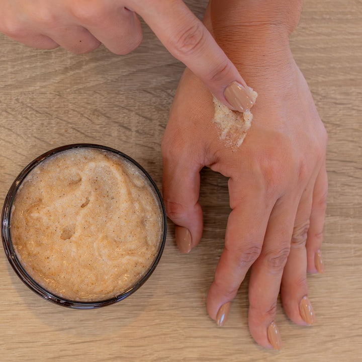 Person applying a brown cream to their hand with a small container of the cream on a wooden surface.
