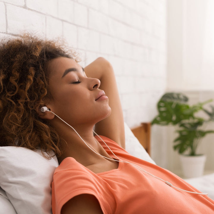 Woman listening to Yaye's Aboriginal meditation audio in bed for relaxation and stress relief.
